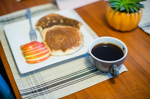 Close up shot of a plate with sweet waffles and coffee served on a tray as a breakfast in bed. There is also a single macaroon and a tulip for decoration.