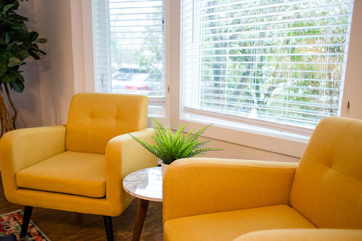 Two yellow arm chairs next to each other in a room with a large window.
