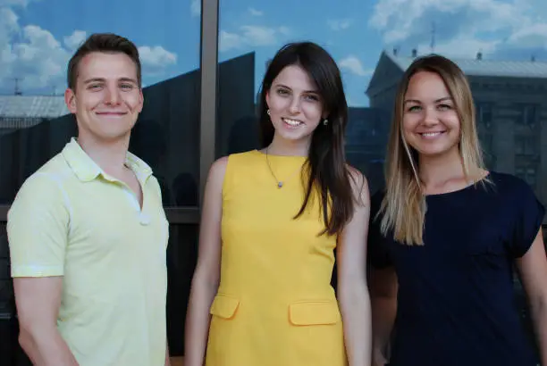 Portrait of the happy smiling man and two beautiful women standing against the mirror office building background. Success concept.