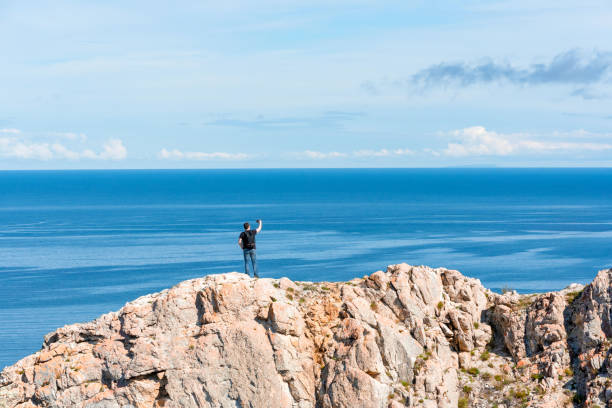 istock Man with backpack standing on a rock at the end of earth using his smartphone for selfie photoshoot. Hiking or travel concept. Exploring the great outdoors. Beauty of nature 1388281720