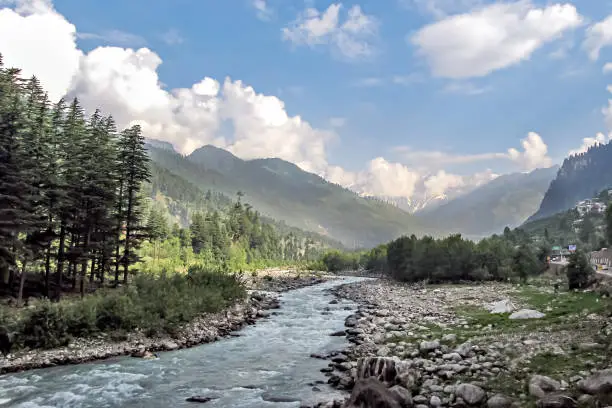 Beas river with snow cladded mountain , blue clouds and greenery in the background