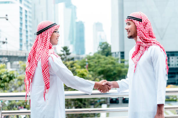 uomo d'affari arabo vestito musulmano che stringe la mano insieme nella moderna città degli emirati arabi uniti. uomini musulmani collaborazione commerciale stretta di mano con partnership. diversità multirazziale persone arabe fiducia impegno - sheik abu dhabi united arab emirates asia foto e immagini stock