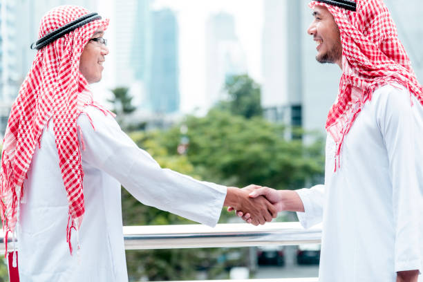 uomo d'affari arabo vestito musulmano stringendo la mano insieme. uomini musulmani lavoro di squadra partner commerciale stretta di mano con partnership commerciale. close up mano diversità emirati arabi uniti persone multirazziali si fidano dell'impegno  - sheik abu dhabi united arab emirates asia foto e immagini stock