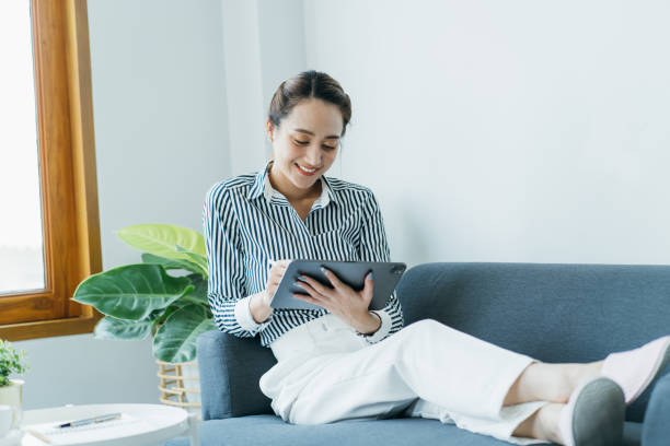 istock Smiling pretty woman using tablet computer while sitting on a sofa at home. 1388290517