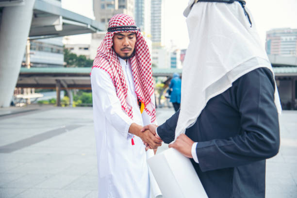 vestito musulmano dell'uomo d'affari arabo che stringe la mano insieme. uomini musulmani lavoro di squadra stretta di mano del partner commerciale con partnership commerciale. mano ravvicinata uae diversità persone multirazziali fiducia onestà impegno - sheik abu dhabi united arab emirates asia foto e immagini stock