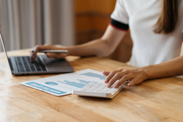 istock Close up woman hand using calculator and writing make note with calculate about cost at home office. 1388296305