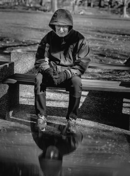 imagem em preto e branco de homem mais velho triste sentado em banco de madeira no parque do centro-oeste em dia frio - bench men puddle sitting - fotografias e filmes do acervo