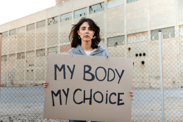giovane donna caucasica che guarda la macchina fotografica con espressione seria tenendo un cartello di cartone: il mio corpo la mia scelta - aborto foto e immagini stock