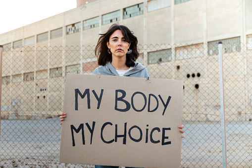 Young caucasian woman looking at camera with serious expression holding a cardboard sign: My body my choice. Feminism activist concept.