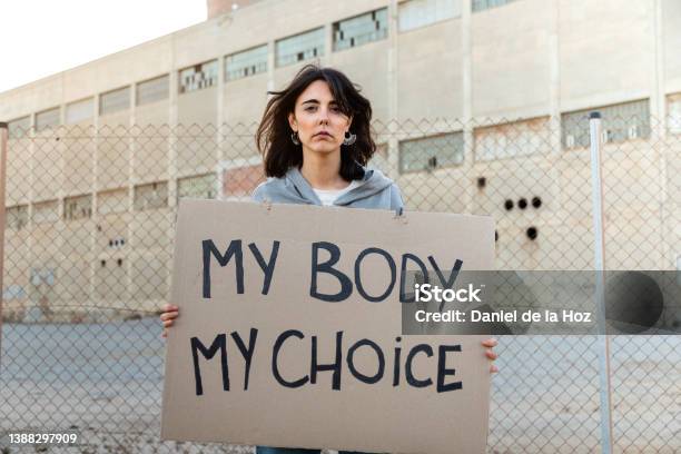 Young Caucasian Woman Looking At Camera With Serious Expression Holding A Cardboard Sign My Body My Choice Stock Photo - Download Image Now