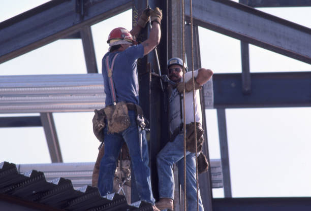 San Diego, California, USA - February 26, 2022: Two ironworkers work on an i-beam on a high rise building.  They are surrounded by the steel girders that will eventually support the building.