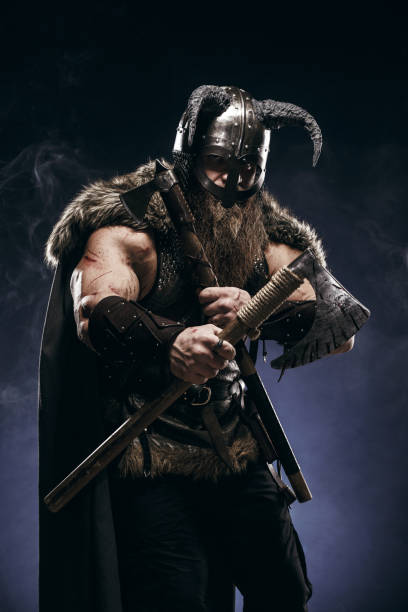 istock Medieval warrior berserk Viking in armor and helmet with horns with axes attacks enemy. Concept historical photo of Scandinavian god 1388302451