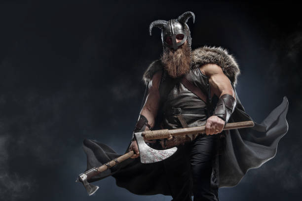 istock Medieval warrior berserk Viking in armor and helmet with horns with axes attacks enemy. Concept historical photo of Scandinavian god 1388302575