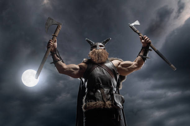 istock Medieval warrior berserk Viking in armor and helmet with horns with axes attacks enemy. Concept historical photo of Scandinavian god 1388303344