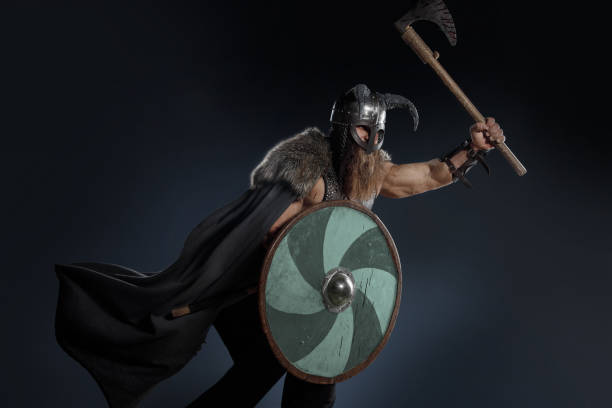 istock Medieval warrior berserk Viking in armor and helmet with horns with axes attacks enemy. Concept historical photo of Scandinavian god 1388303435