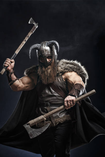 istock Medieval warrior berserk Viking in armor and helmet with horns with axes attacks enemy. Concept historical photo of Scandinavian god 1388304200