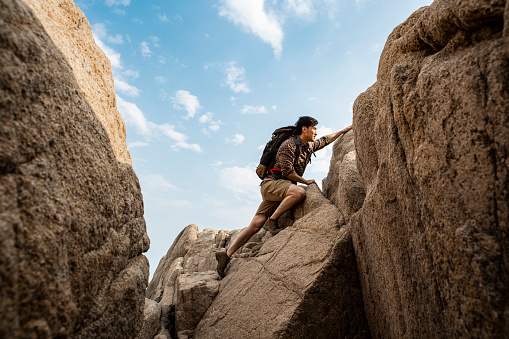 A mountaineer is struggling up the steep rocky valley. Portrait.