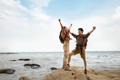 A couple of hiker raise their hands in celebration after landing on destination island. Portrait.