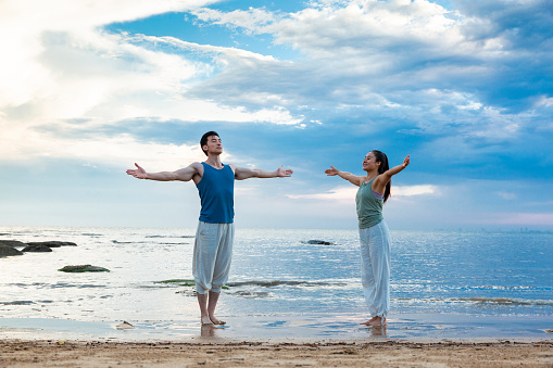 Young couple practicing yoga meditation while standing on the beach - stock photo