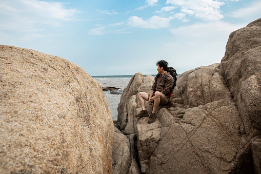 A young outdoorsman is sitting on a rock overlooking the sea. Portrait.