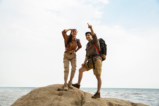 Two lovers of hiking is successfully landing on the island, ready to move on to their next destination. The man is pointing into the distance and the woman is watching with blocking the light from her eyes. Portrait.