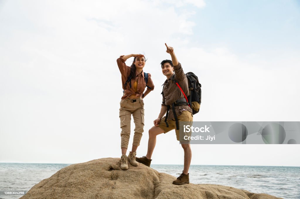 Two hikers exploring their next destination - stock photo Two lovers of hiking is successfully landing on the island, ready to move on to their next destination. The man is pointing into the distance and the woman is watching with blocking the light from her eyes. Portrait. Hiking Stock Photo