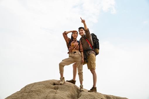 Two lovers of hiking is successfully landing on the island, ready to move on to their next destination. The man is pointing into the distance and the woman is watching with blocking the light from her eyes. Portrait.