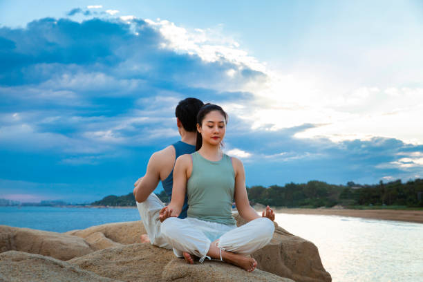Couples practicing yoga mindfulness on island rocks - stock photo
