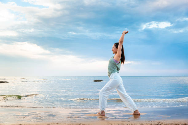 istock Young woman practicing stretching using a resistance band on the beach - stock photo 1388304384