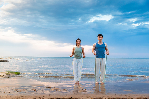 Young couple using resistance bands for yoga stretch at the beach - stock photo
