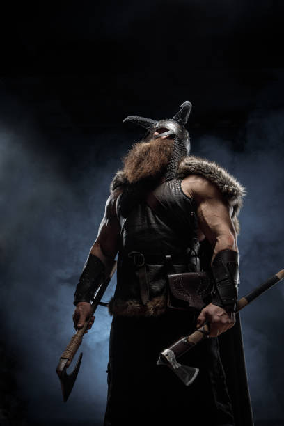 istock Medieval warrior berserk Viking in armor and helmet with horns with axes attacks enemy. Concept historical photo of Scandinavian god 1388304485