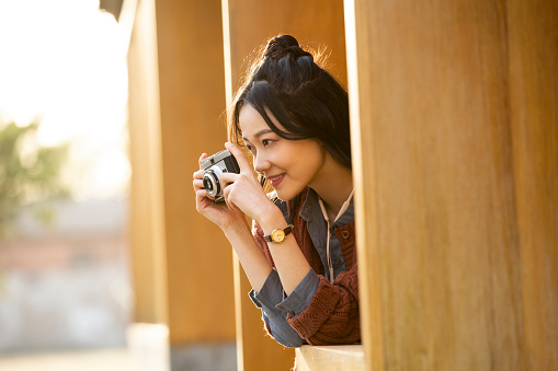 A young Chinese photographer is taking pictures from the window ledge of a building. Portrait.