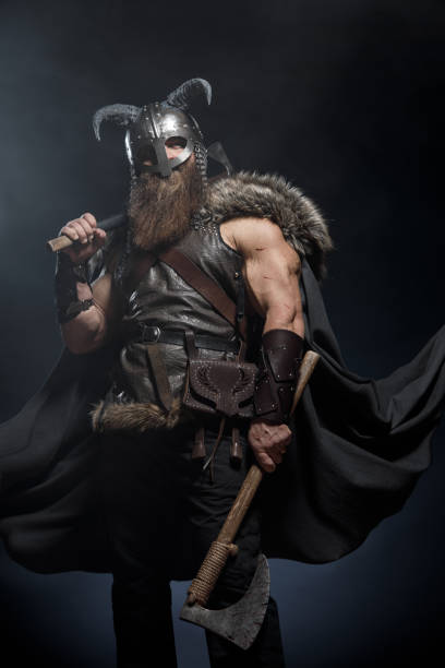 istock Medieval warrior berserk Viking in armor and helmet with horns with axes attacks enemy. Concept historical photo of Scandinavian god 1388304677