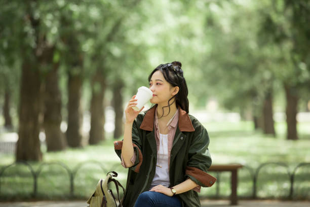 young female tourist drinking coffee on a bench - stock photo - hair bun asian ethnicity profile women imagens e fotografias de stock