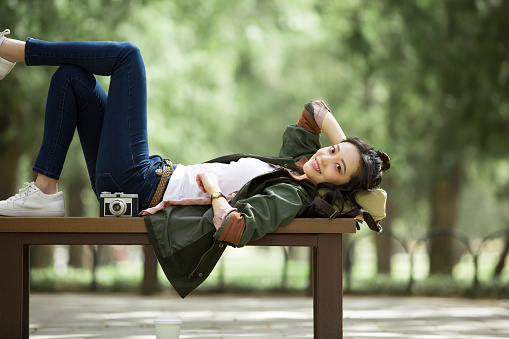 A young female photographer is lying and resting on a bench in a forest park. Portrait.