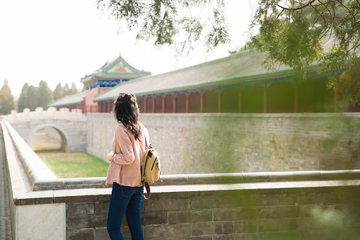 A young female tourist is walking on the ancient city wall. Rear View.