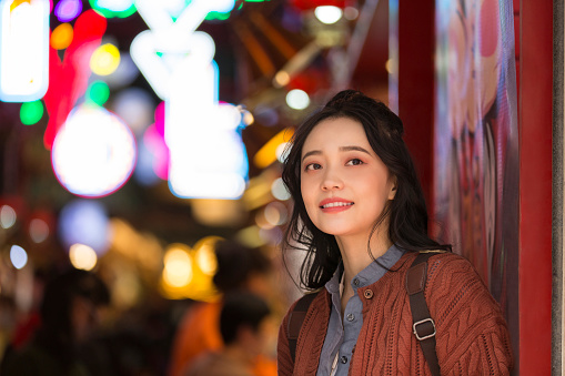 A young female college student is enjoying the scenery at a neon night market in Beijing. Portrait.