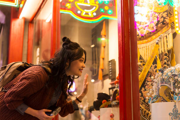 Young Chinese college girl marvelling beside show window of Peking Opera costumes and headdresses - stock photo A young Female college student in China is marvelling at ancient culture outside the show window of Peking Opera costumes and headdresses. Portrait. historical museum stock pictures, royalty-free photos & images