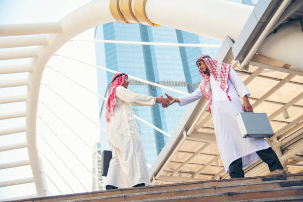 vestito musulmano dell'uomo d'affari arabo che stringe la mano insieme nello sfondo moderno della città degli emirati arabi uniti. uomini musulmani lavoro di squadra stretta di mano partner commerciale con partnership. diversità multirazziale arabo fiduc - sheik abu dhabi united arab emirates asia foto e immagini stock