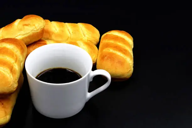 Butterbread next to a cup of coffee with a black background