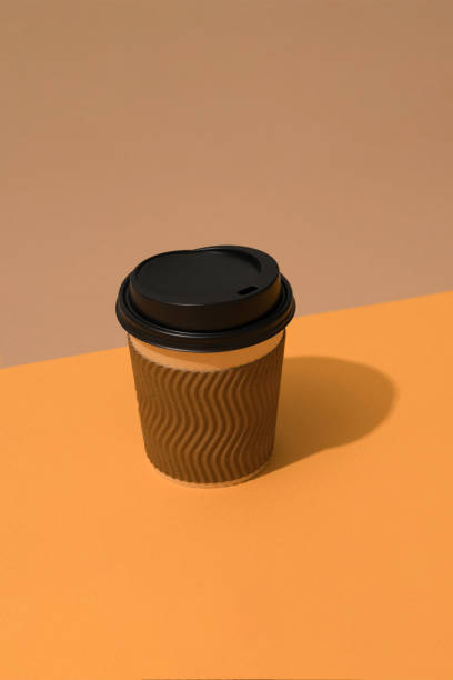 istock Brown eco coffee cup with black plastic lid on orange and brown background with copy space. Vertical composition 1388312137