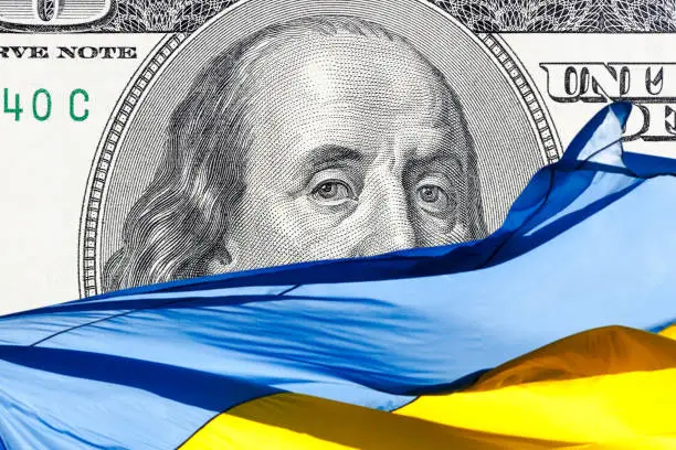 Photo of ukrainian national flag on foreground and US one hundred dollars paper currency on background. ukraine investment concept