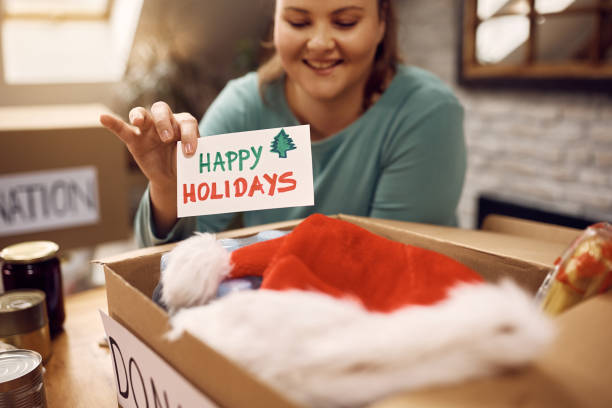 istock Close-up of woman adding greeting card while packing donation boxes for holidays. 1388314110