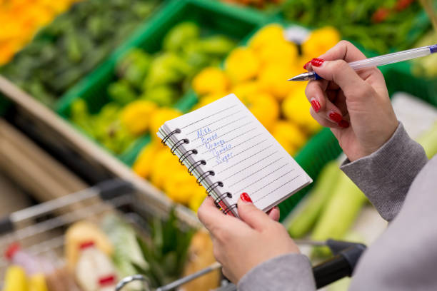 femme avec ordinateur portable en épicerie, agrandi. liste de courses sur papier. - liste de courses photos et images de collection