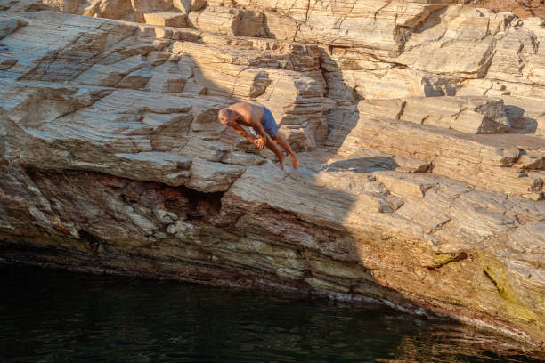 Mid adult man in trunks leaping head-up off a rocky cliff into sea water in natural pool