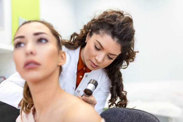 istock Dermatologist in latex gloves holding dermatoscope while examining attractive patient with skin disease. Female dermatologist examining patient with dermascope, looking for signs of skin cancer. 1388320929
