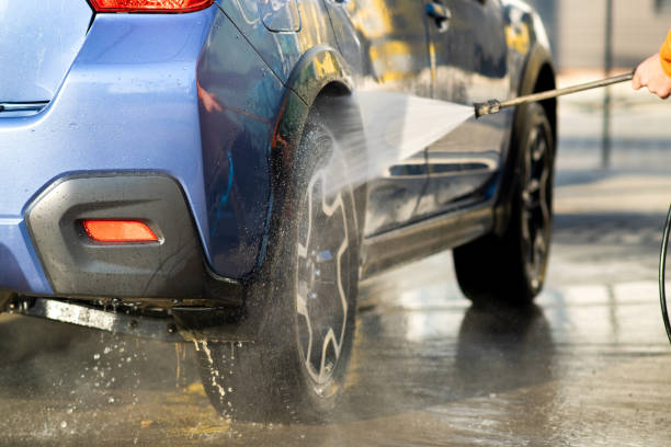 nahaufnahme des männlichen fahrers waschen sein auto mit kontaktlosen hochdruck-wasserstrahl in selbstbedienung autowäsche. - autowaschanlage stock-fotos und bilder