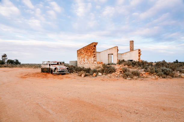 The remains of  an old stone home slowly crumbling away, beside it sits a vintage car slowly rusting under the harsh Australian sun on the inland desert of Australia.  Remnants of a bygone era
