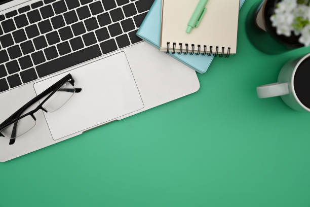 istock Computer laptop, notepad eyeglasses and coffee cup on green background. Top view. 1388324881