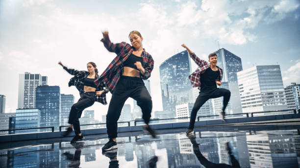 istock Diverse Group of Three Professional Dancers Performing a Hip Hop Dance Routine in Front of a Big Digital Led Wall Screen with Modern Urban Skyline with Skyscrapers in Studio Environment. 1388326400